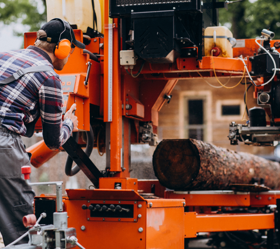 Worker operating huge lumber sawing machine.