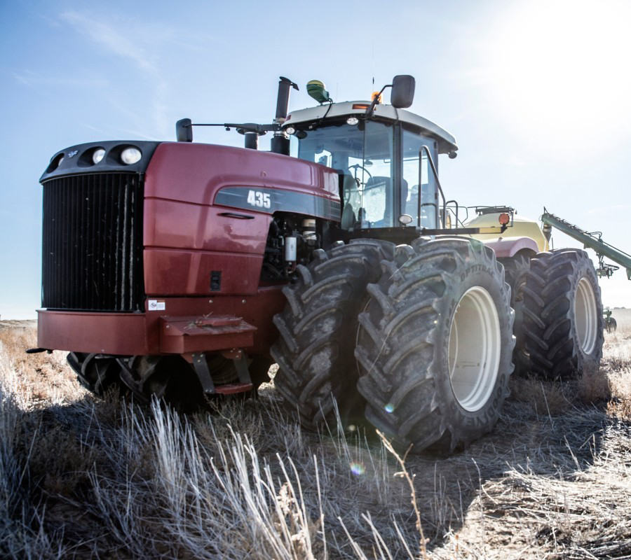 Red tractor with large dual tires parked in a dry field under a bright sky.