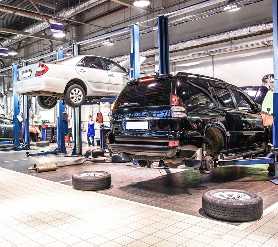 A mechanic is repairing a car inside a well-equipped garage, surrounded by equipment.