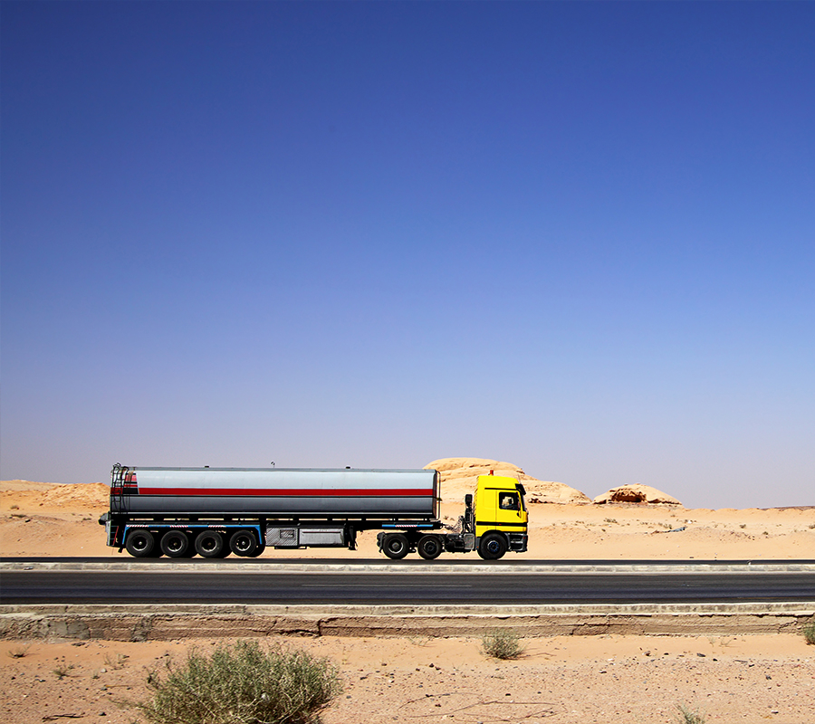 A tanker truck moves steadily on a remote desert road.