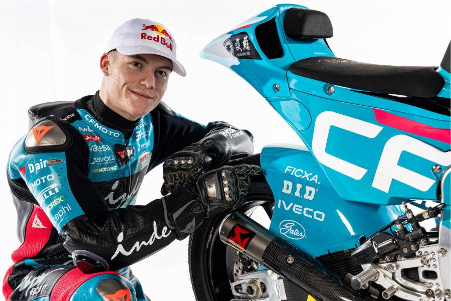 Motorcycle racer leaning beside a blue race bike