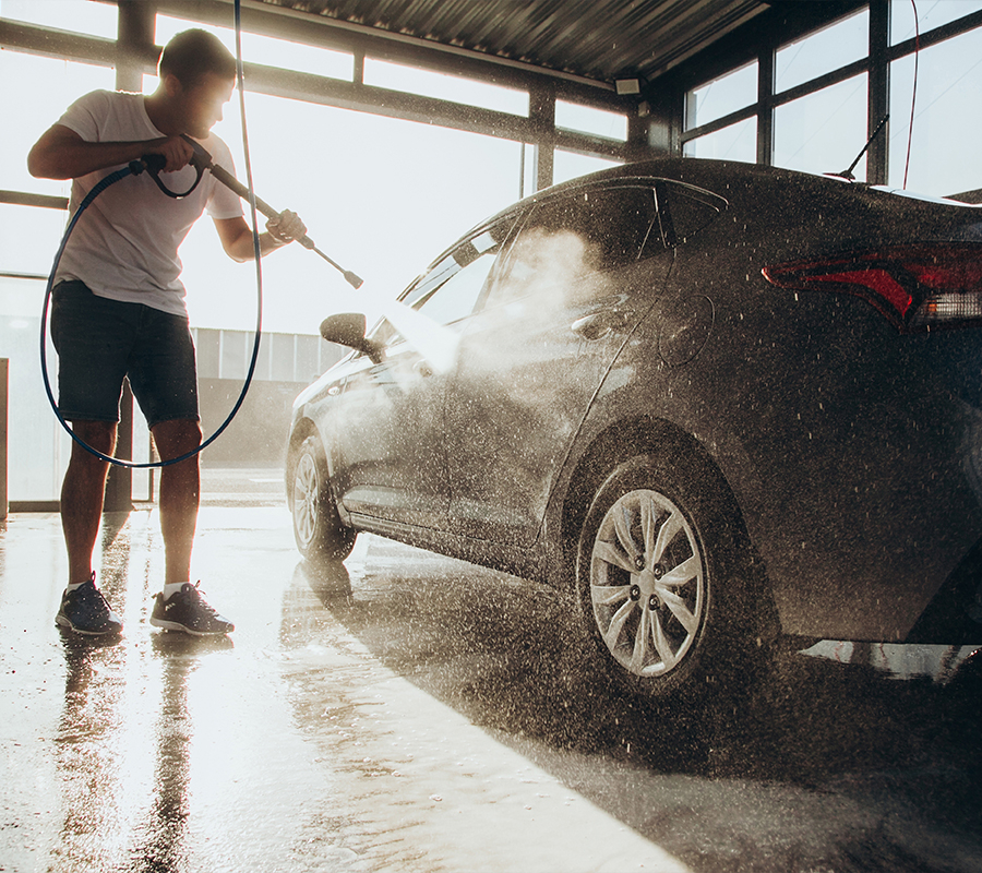 A man uses a pressure washer to clean his car, spraying water with a hose for a shiny finish.