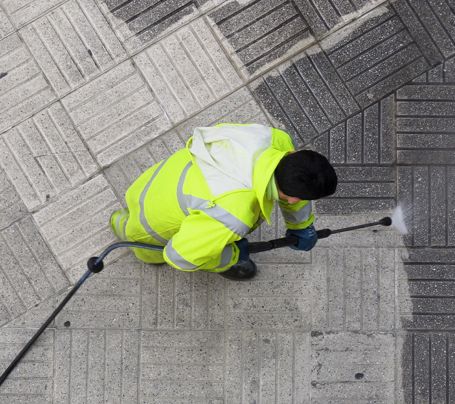 A man in a bright yellow jacket is busy cleaning the sidewalk, making the area look neat and tidy.