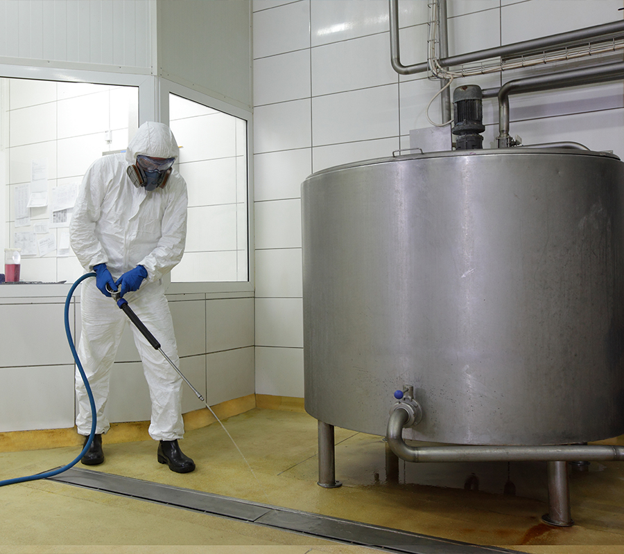 A man in a white suit and protective gear sprays water on a tank, ensuring safety and cleanliness in the process.