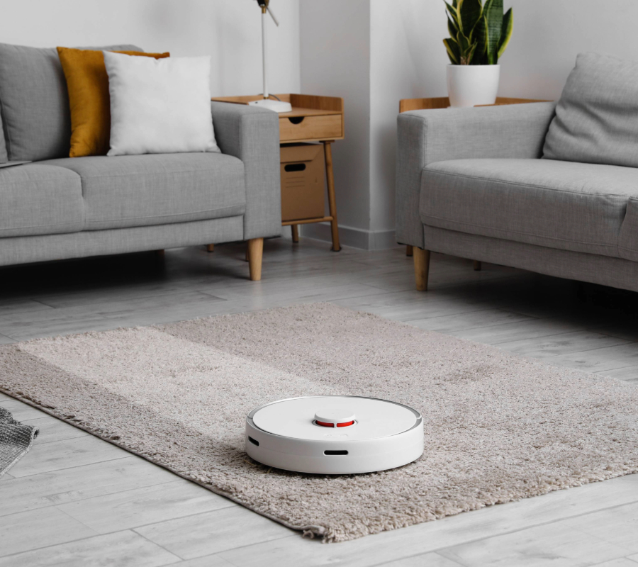Smart robot vacuum cleaner operating on a beige rug between two grey sofas in a modern living room.