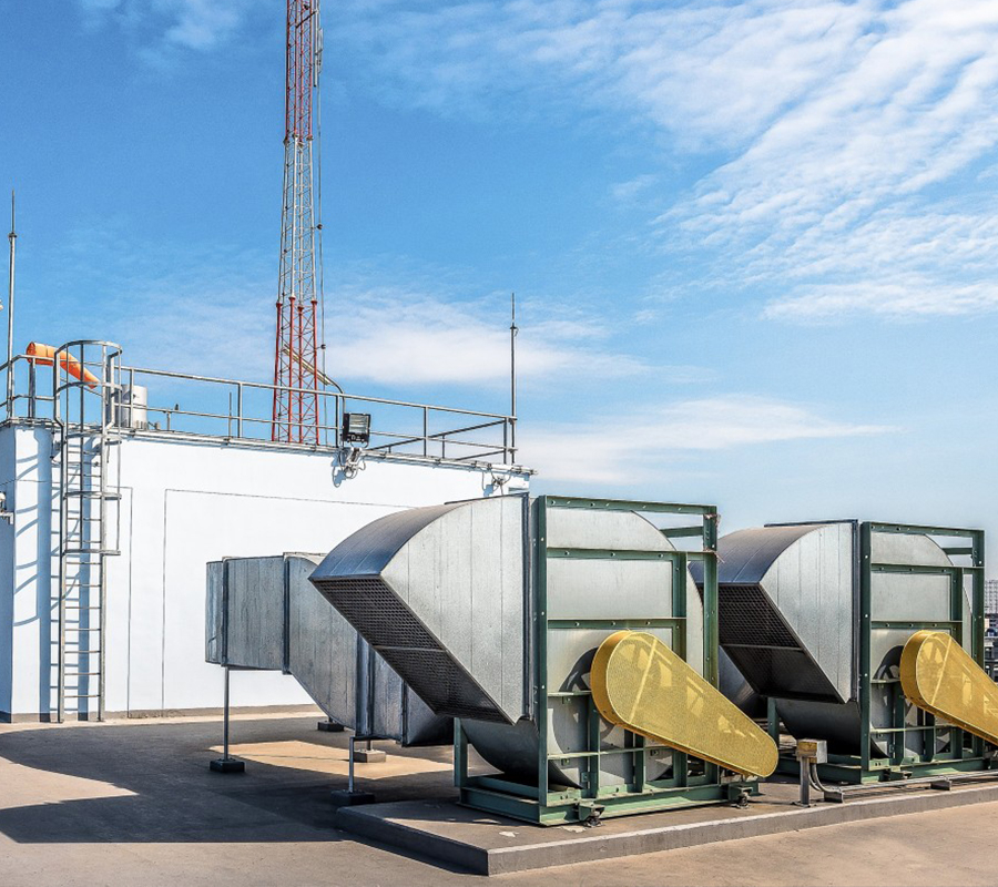 A cluster of air conditioning units on a roof, with a tall tower standing nearby, all under a clear blue sky.