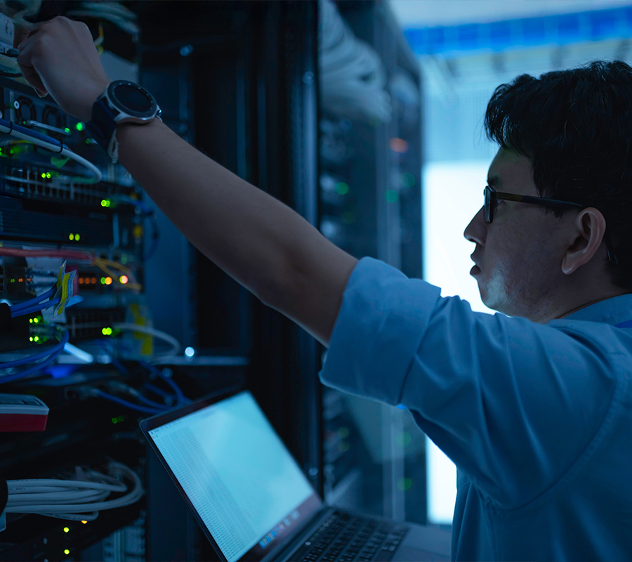 male technician in a white shirt reaches up to service a data center rack