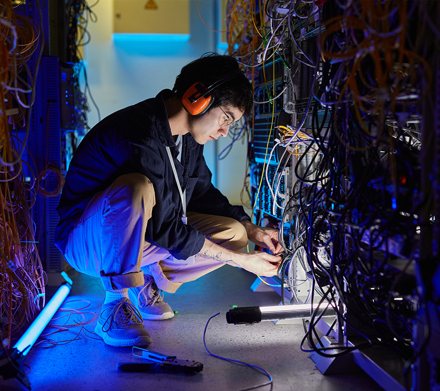 male technician crouches between server racks to adjust a bundle of wires