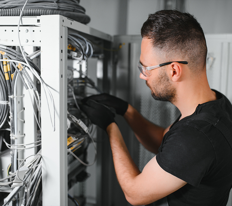 male technician with safety glasses and black gloves reaches in to service a data center rack