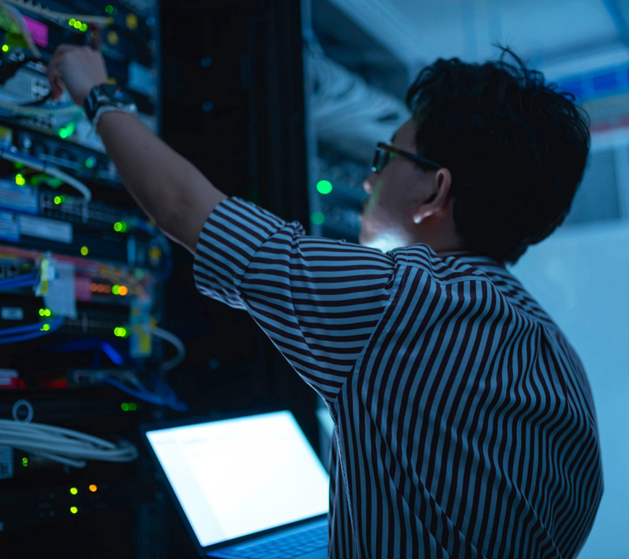 IT technician adjusting cables in a server rack with a laptop nearby