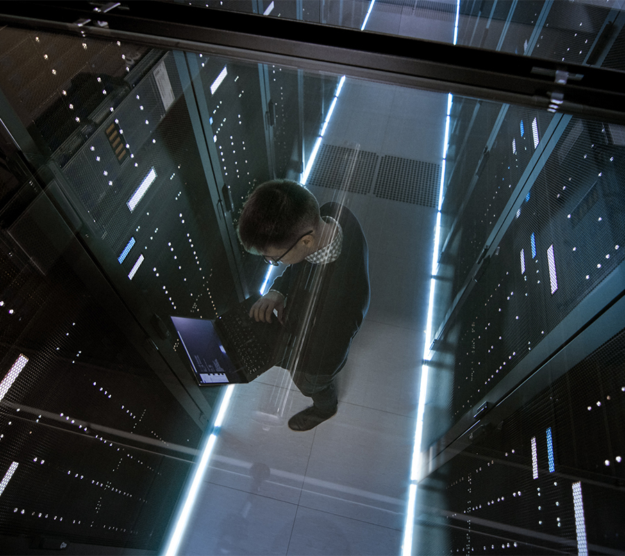 A man stands in a server room, using a laptop amidst in-row and in-rack cooling systems.