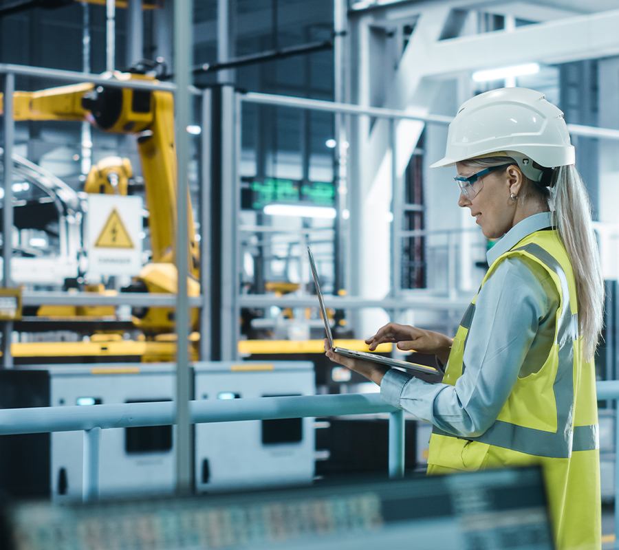 A woman in a hard hat and safety vest operates a tablet, demonstrating safety and technology in a work environment.