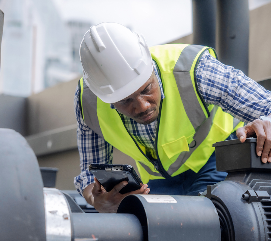 A man with a hard hat and safety vest reviews a device, prioritizing safety, technology, and equipment performance.