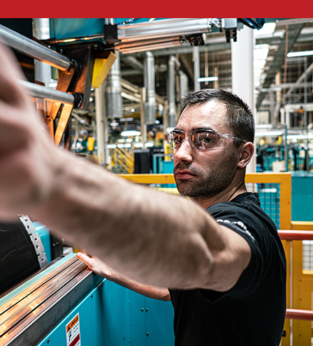 A man wearing safety goggles looking at a piece of machinery.