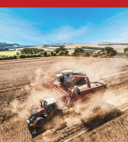 Red tractor and combine harvester working together in a dusty field during harvest on a sunny day