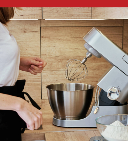 Person standing next to a silver stand mixer with a whisk attachment in a modern kitchen.