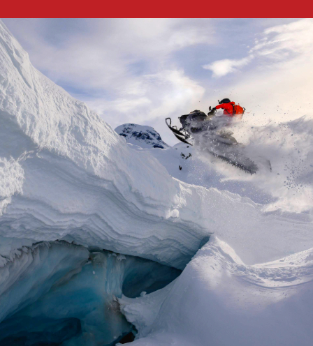 Snowmobiler leaping over a snowy ridge