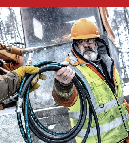 Man holding hydraulic hose in snowy jobsite.