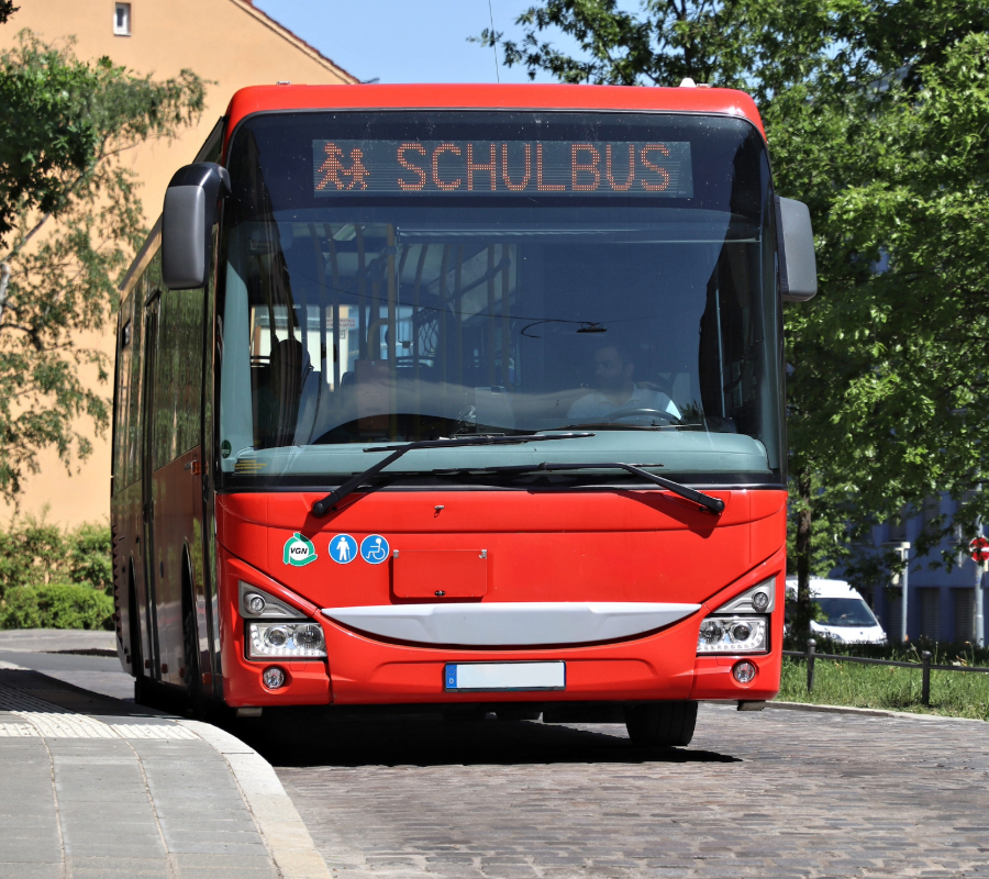 Red school bus with “Schulbus” displayed on the front sign, parked on a street.