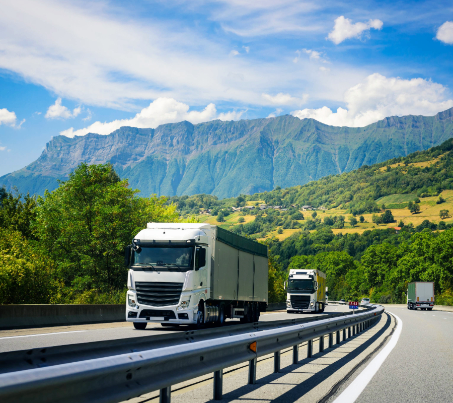 White semi-trucks driving on a highway with green mountains in the background.