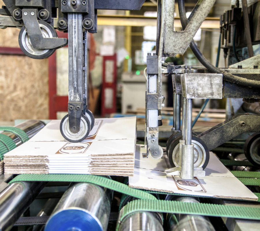 Corrugated cardboard being cut and folded by industrial packaging machinery on a conveyor belt.