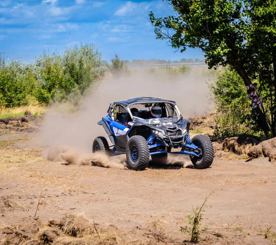 Blue UTV racing through dirt, kicking up dust