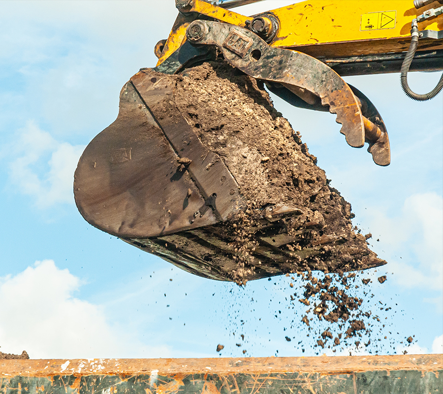 Excavator dumping dirt into hole at construction site.