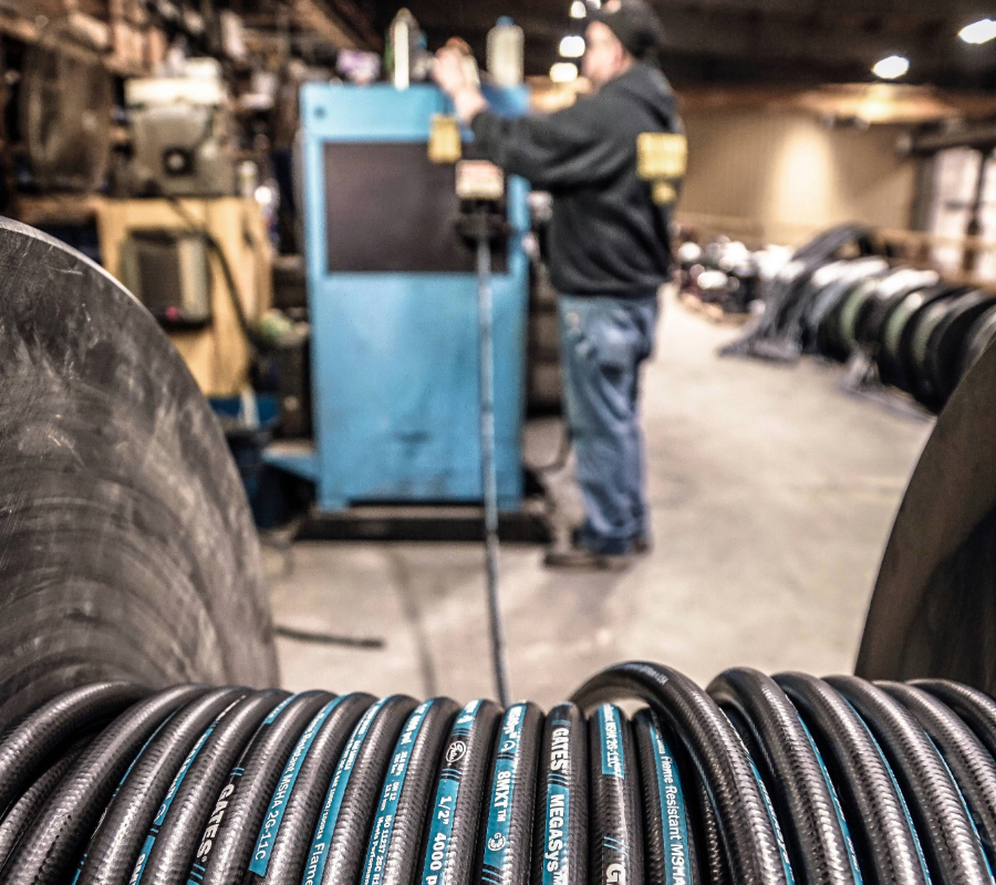 Coiled Gates MegaSys MXT hydraulic hoses in a factory with a technician working in the background.