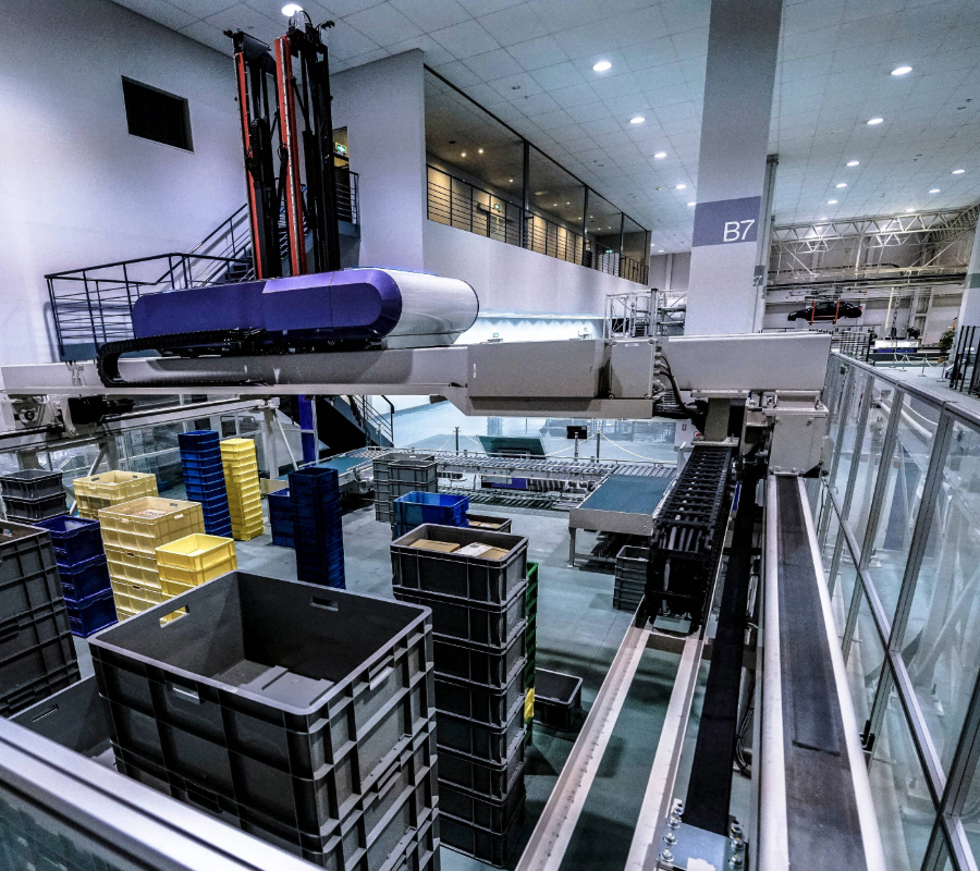 Automated warehouse system with conveyor belts, robotic equipment, and stacked plastic bins for material handling.