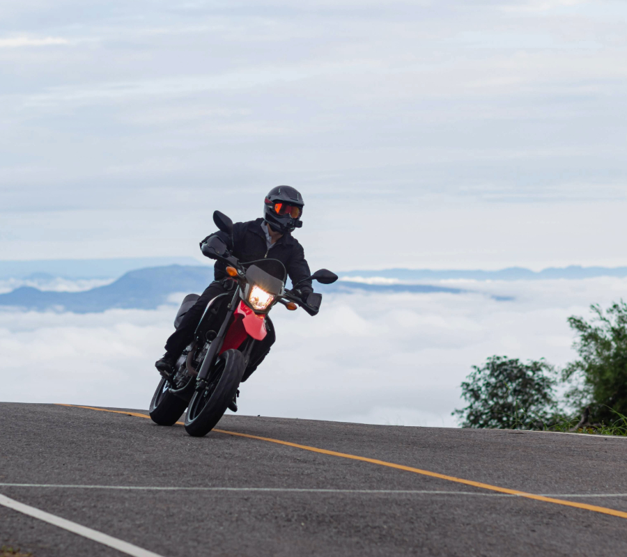 Motorcyclist riding a motorcycle on a paved road behind the sea of fog and mountain peaks