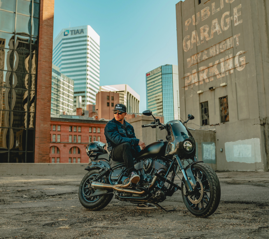 A man sitting on a black motorcycle in an urban setting with tall buildings in the background