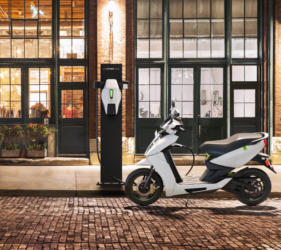 An electric scooter parked at a charging station in front of a stylish urban storefront at night