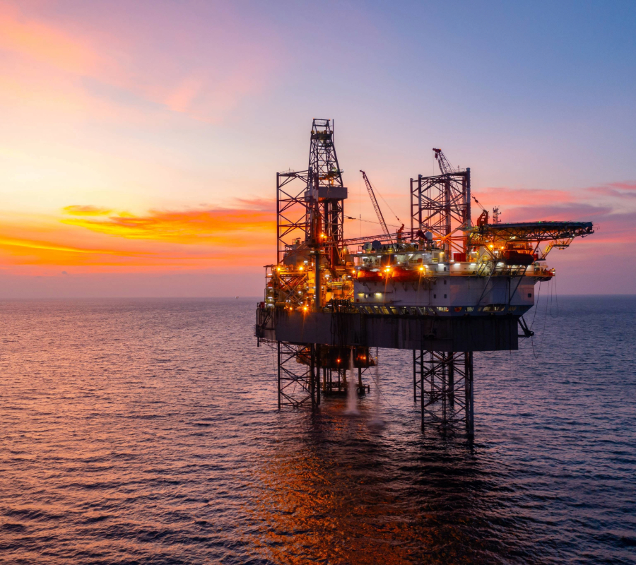 Offshore oil drilling platform illuminated at sunset, with cranes and towers reflecting light over the ocean