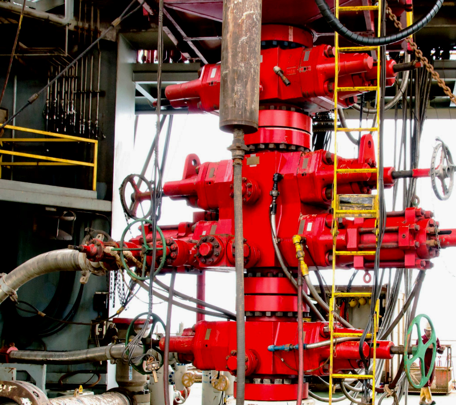 Close-up of red blowout preventer stack with multiple valves, hoses, and control lines on an oil drilling rig