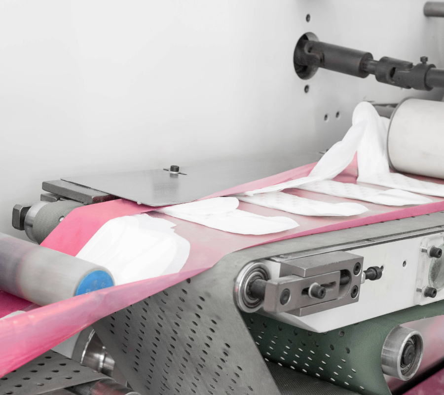 Automated production line machine manufacturing sanitary diapers on a conveyor system.