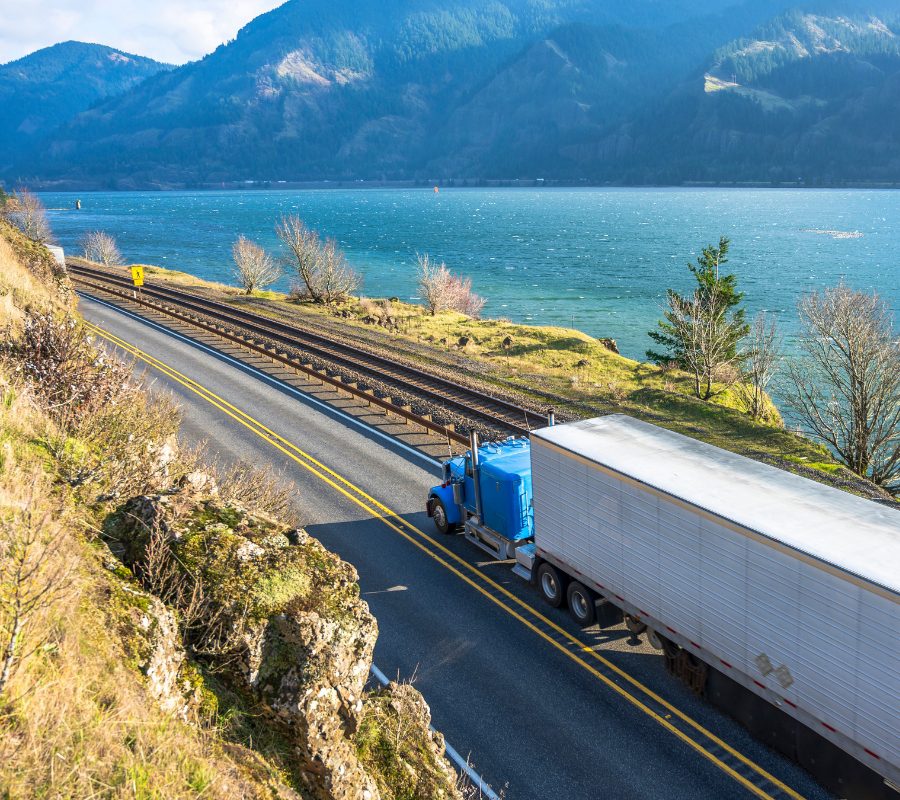 Blue semi-truck driving along a scenic lakeside
