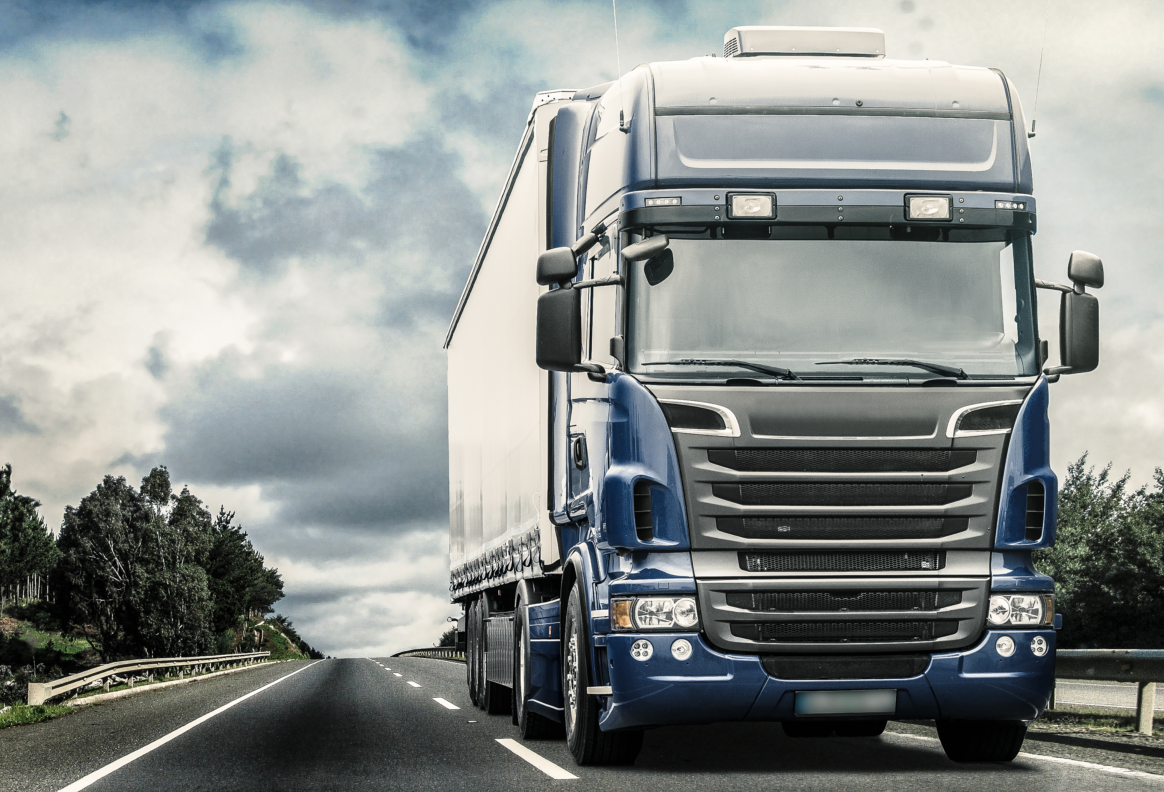 Blue Semi trailer truck on a road with clouds in background