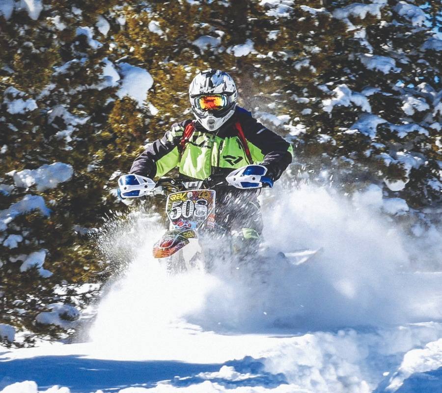 Snowmobile rider speeding through a snowy forest.