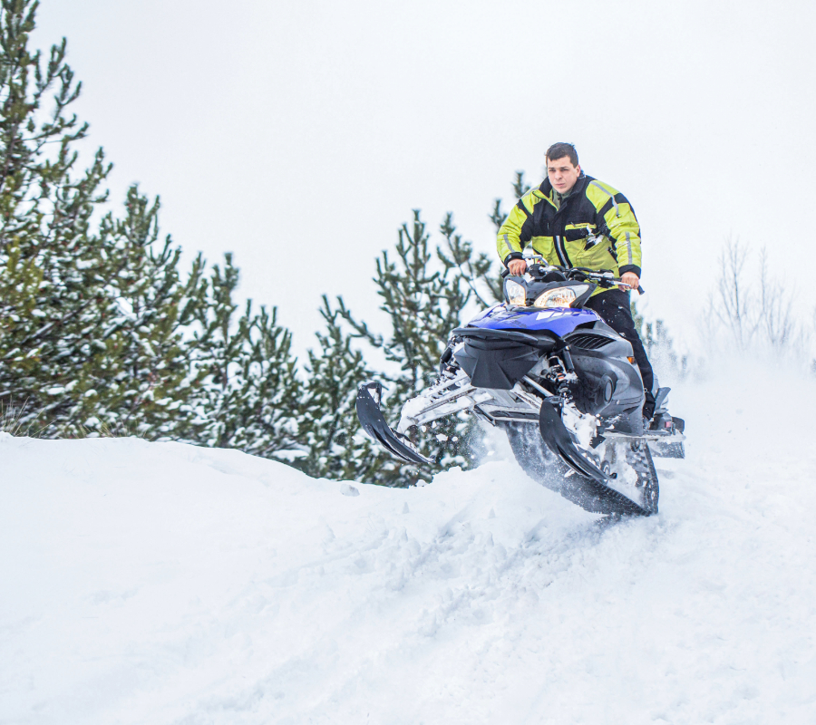 Two ATV riders on a snowy forest trail.