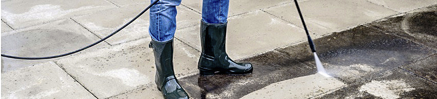 Bottom half of person wearing blackrubber boots holding pressurer washer wand
