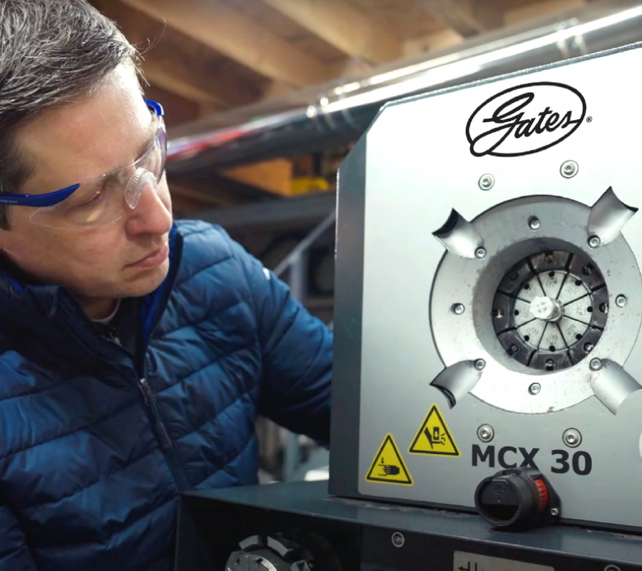 Worker wearing safety glasses operating a Gates MCX 30 crimping machine.