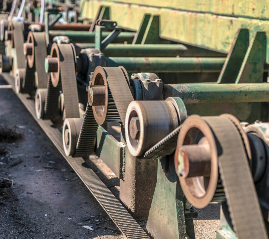 Close-up of an industrial conveyor system with multiple pulleys and drive belts powering heavy machinery.
